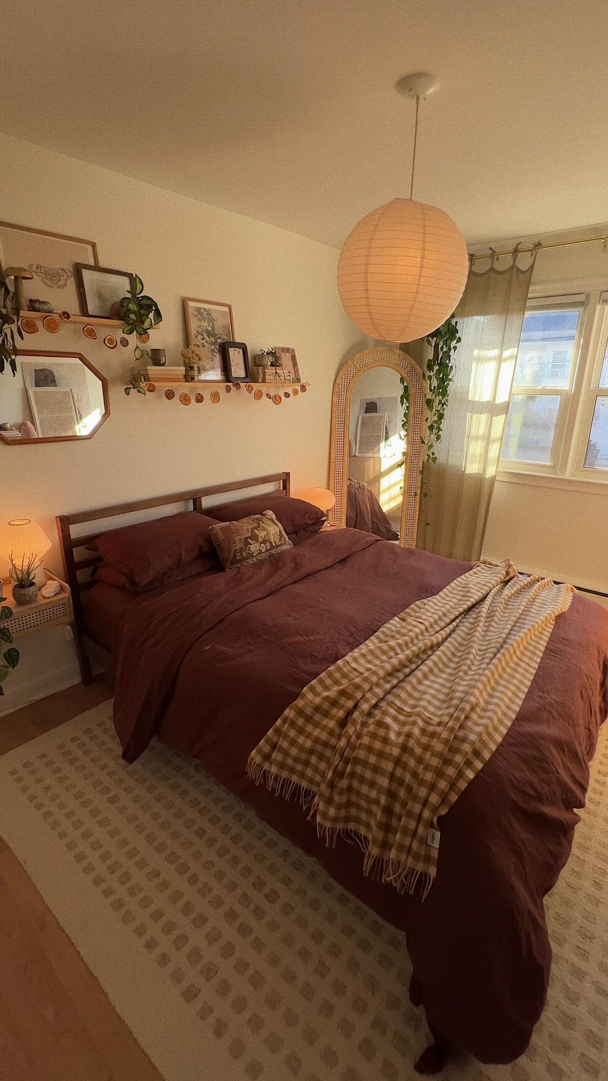 A cozy bedroom with dark brown bedding, a patterned throw, and a large paper lantern hanging above.