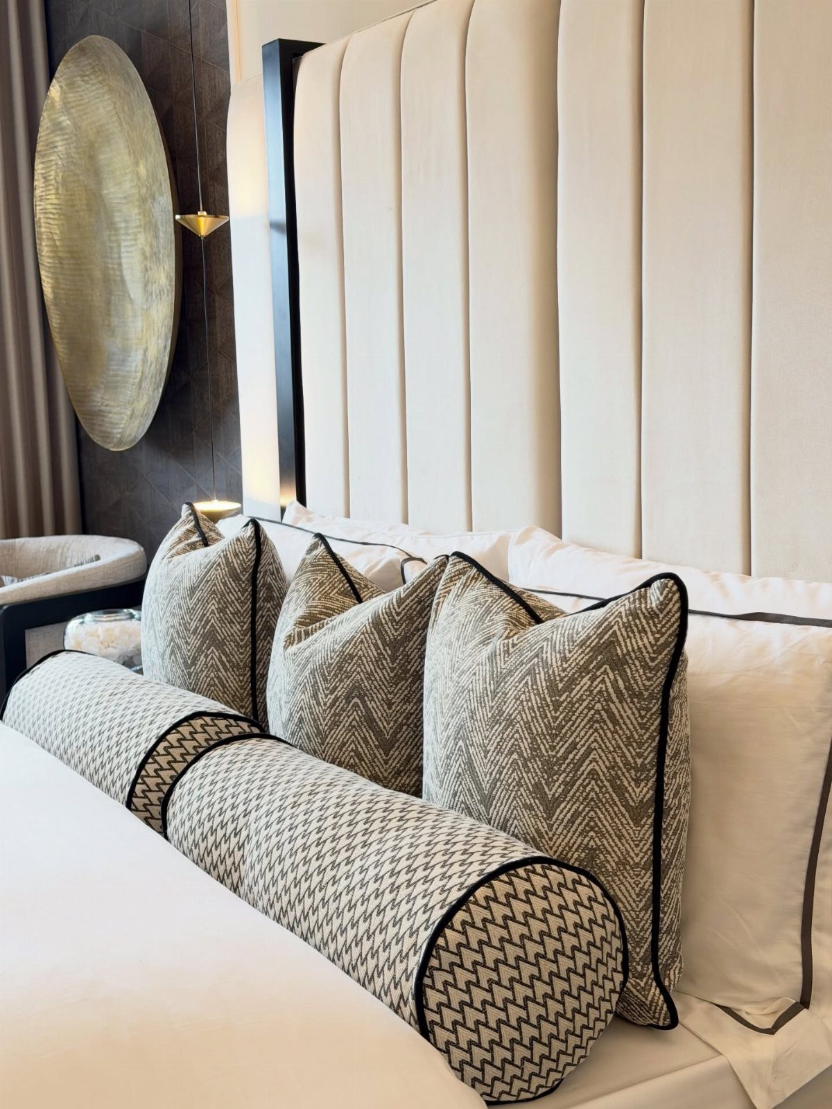 Cream channeled headboard with patterned pillows and a large gold circular wall decor.