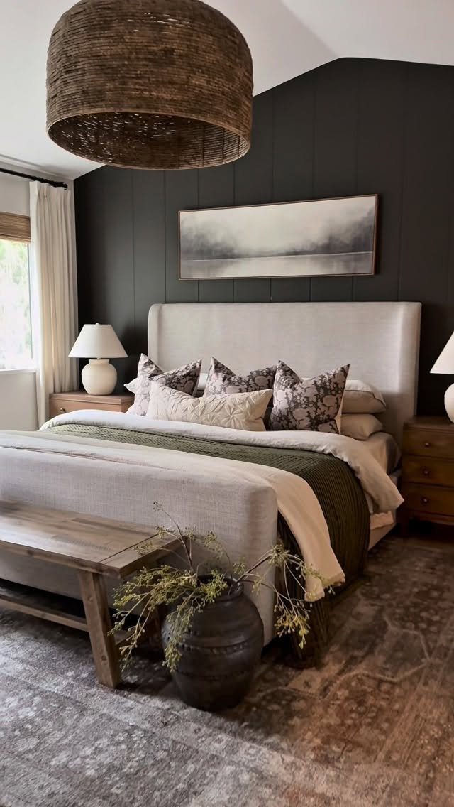 A cozy bedroom with a light upholstered bed, dark paneled walls, and a large woven pendant light.