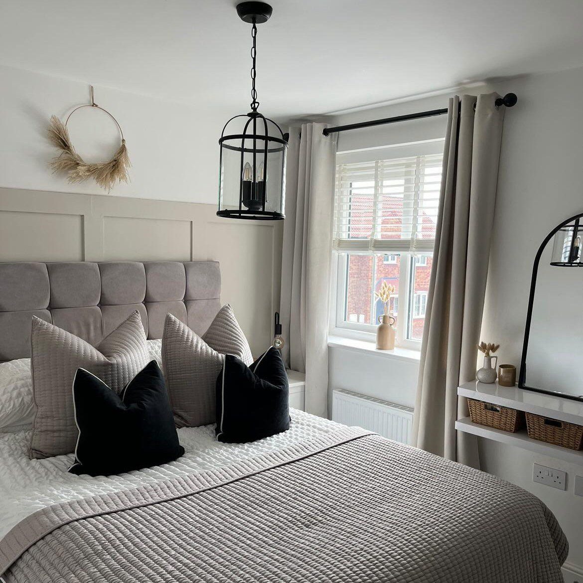 A bedroom with cream bedding, black accent pillows, and a black lantern pendant light.