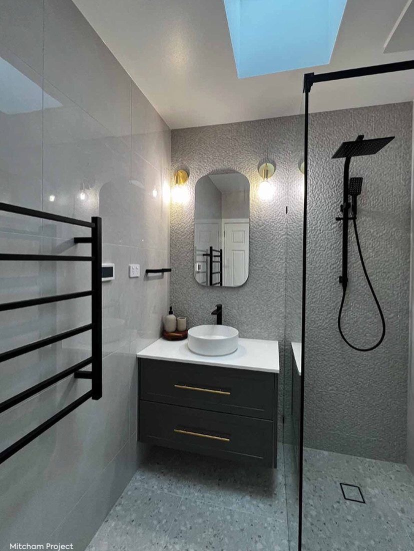Modern bathroom with black vanity, gold hardware, white vessel sink, and grey textured walls.