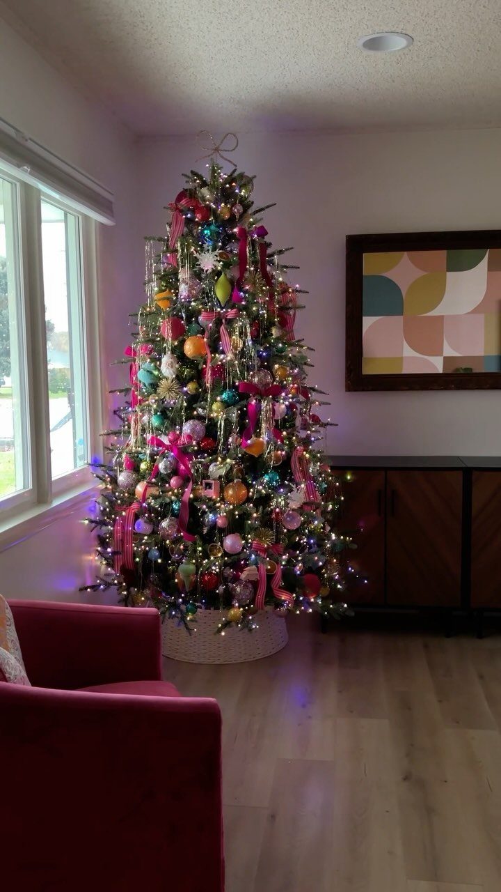 A black Christmas tree decorated with many bright, colorful ornaments and sparkling lights in a room.