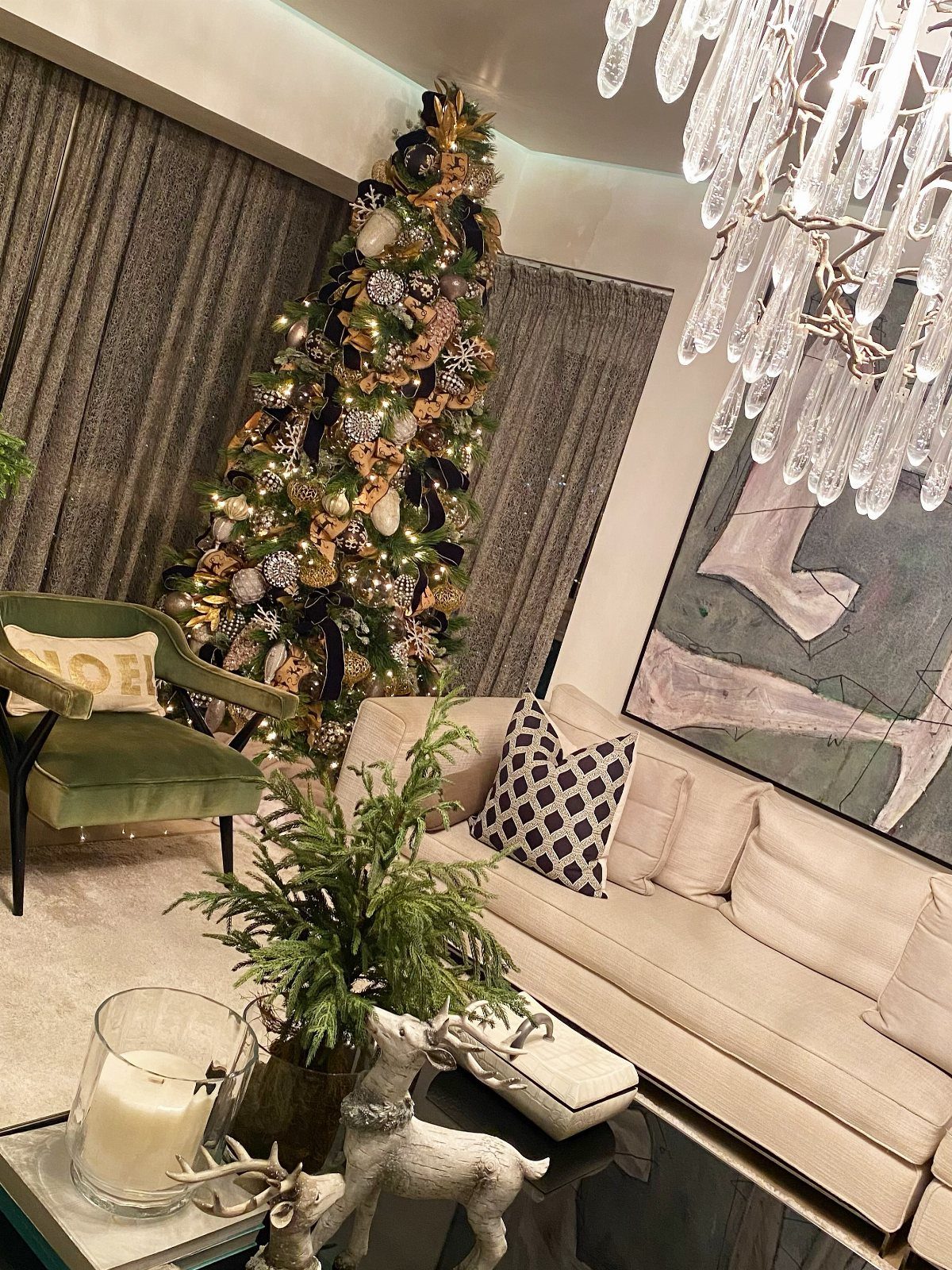 Decorated black Christmas tree with gold ornaments and lights in a modern living room setting.