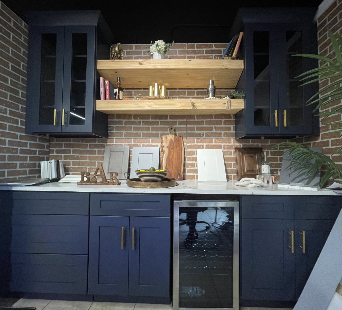 Navy blue kitchen cabinets with natural wood floating shelves against an exposed brick wall.