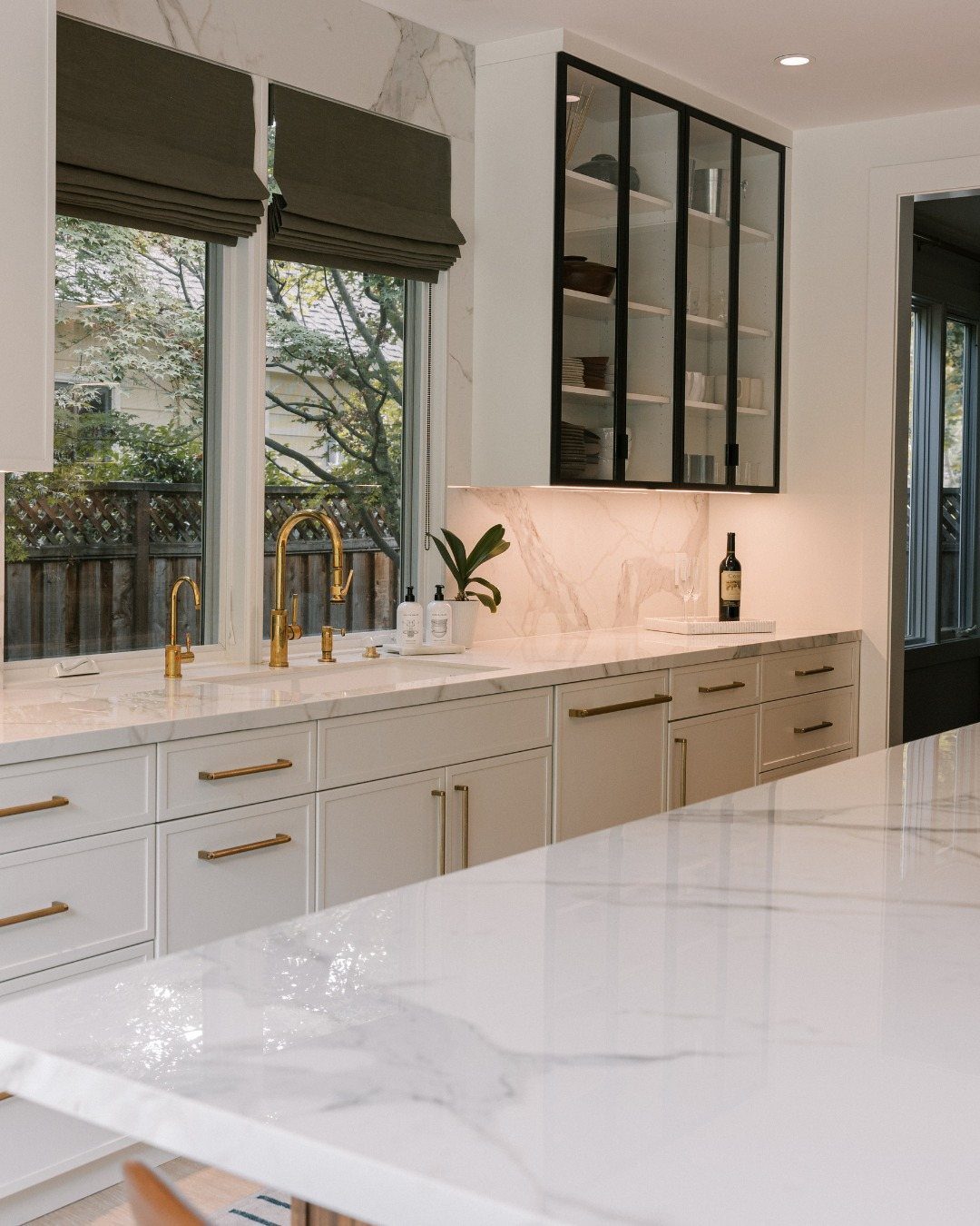 White kitchen cabinets with gold hardware and a black glass insert cabinet above marble countertops.