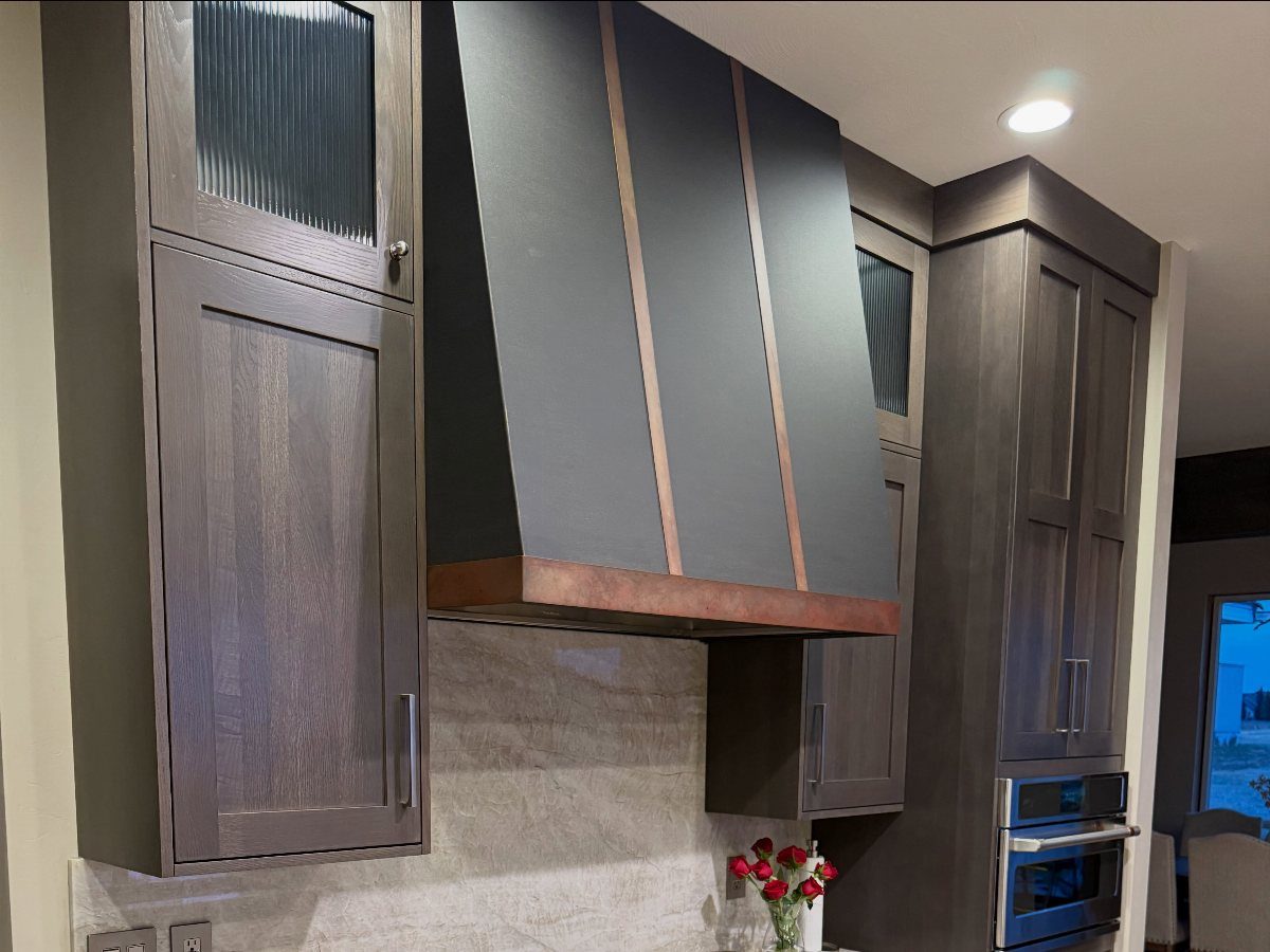 Dark kitchen cabinets with a large black range hood featuring metallic trim and stone backsplash.