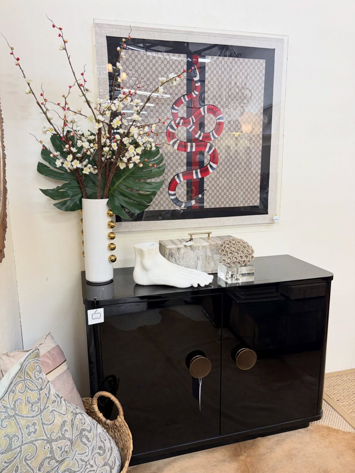 High-gloss black cabinet with gold hardware decorated with floral arrangements and white sculptures.