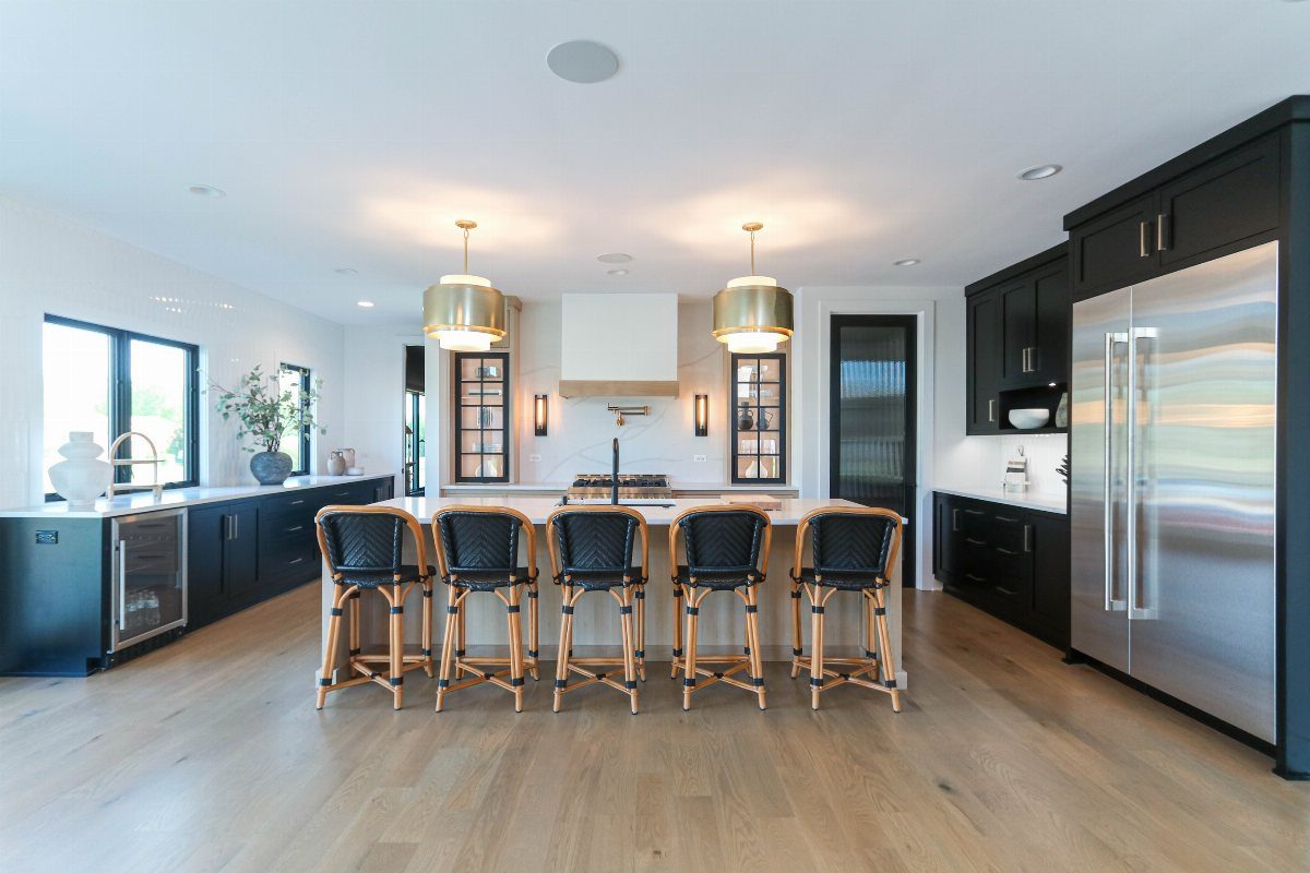 Modern kitchen with black cabinets, marble island, gold pendant lights, and stainless steel appliances.