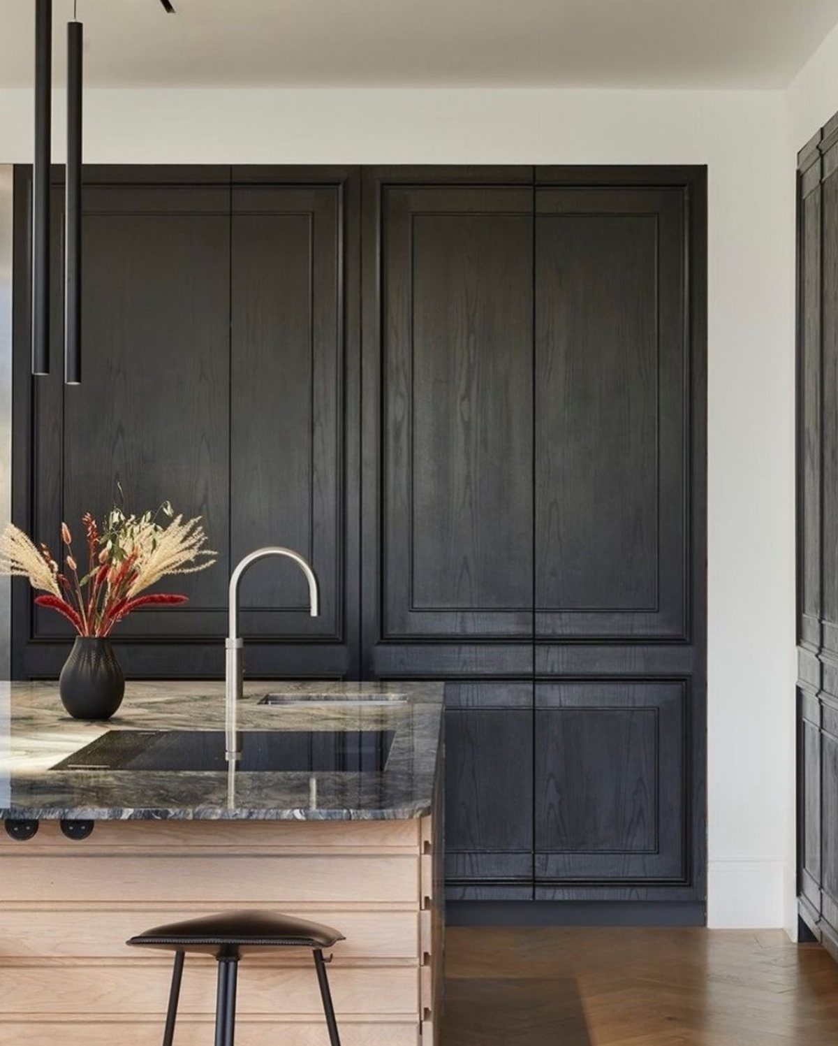 Matte black paneled kitchen cabinets with a marble countertop and silver faucet.