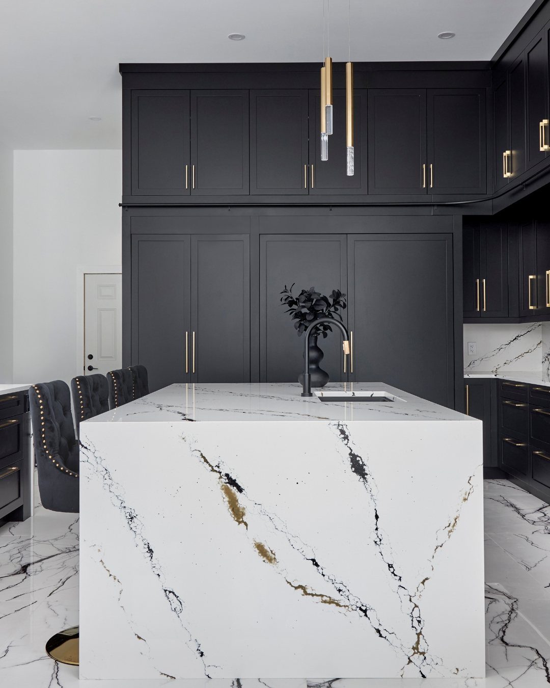Matte black kitchen cabinets with gold hardware and a white marble waterfall island.