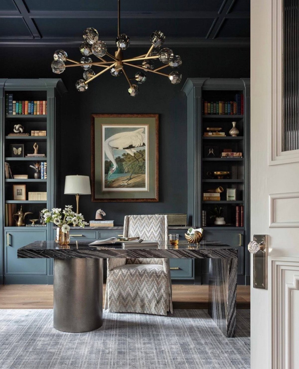Navy built-in bookshelves filled with books in a dark blue home office with a marble desk.
