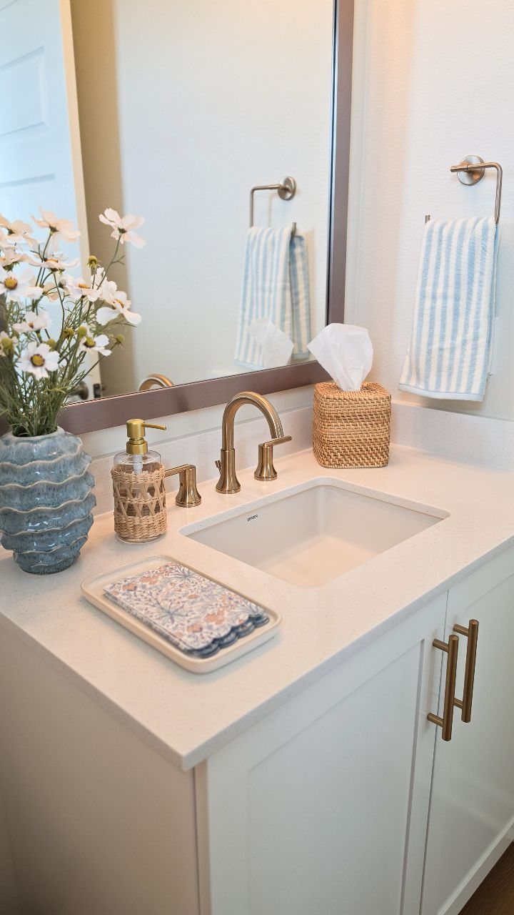 White bathroom vanity featuring gold fixtures, blue floral accents, and a patterned hand towel.