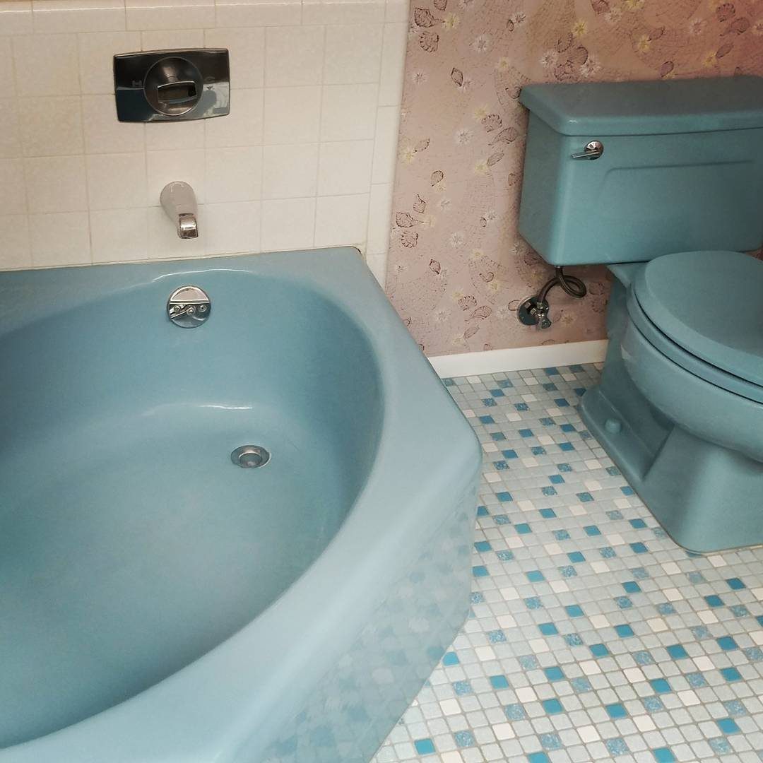 Light blue bathtub and toilet set against floral wallpaper and mosaic tile flooring.