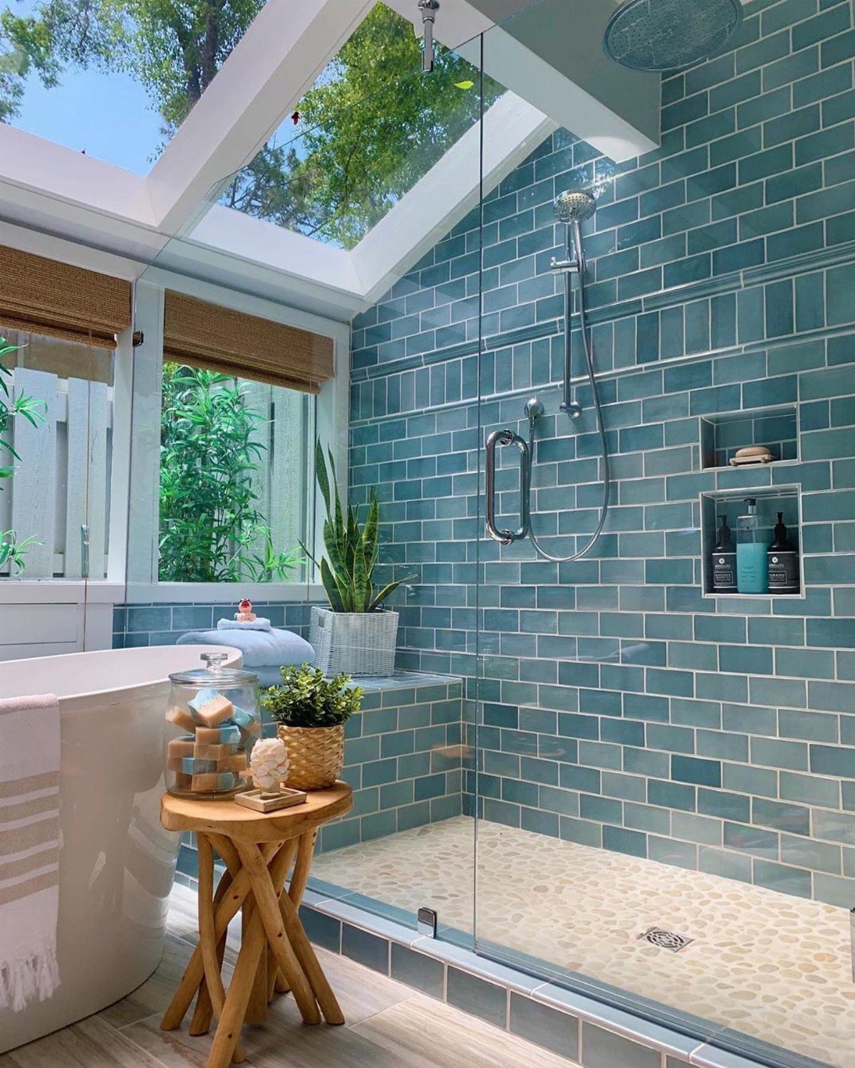 Teal blue subway tiles in a bright walk-in shower next to a white bathtub.