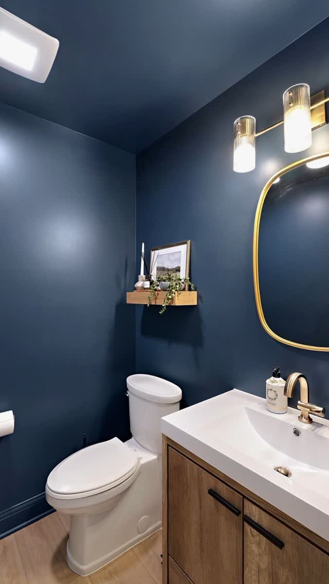 Dark navy blue walls and ceiling in a modern bathroom with a white toilet and vanity.