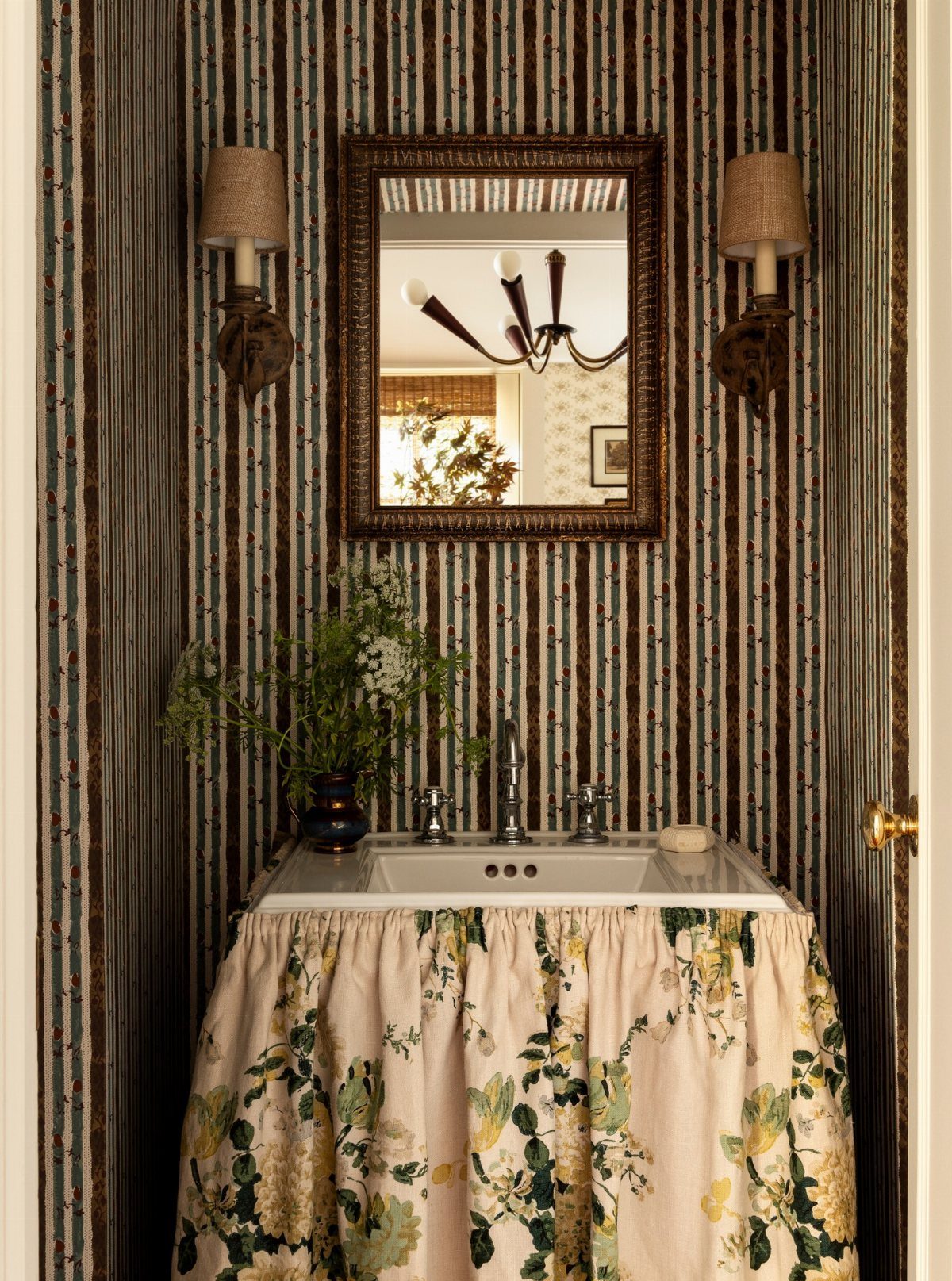 A white sink with a floral fabric skirt against blue ticking stripe wallpaper.