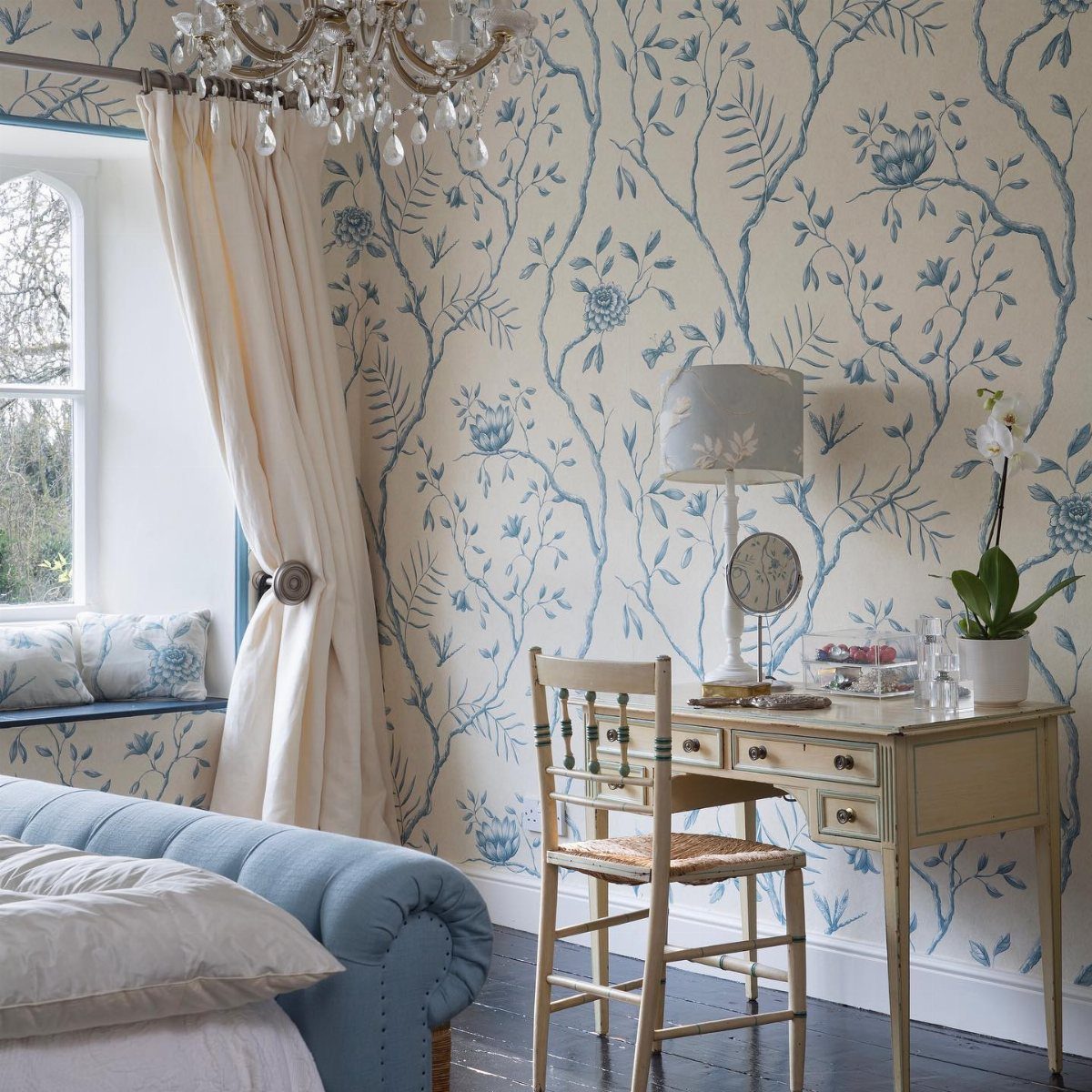 Blue floral patterned wallpaper in a bedroom with a blue bed and a small wooden desk.