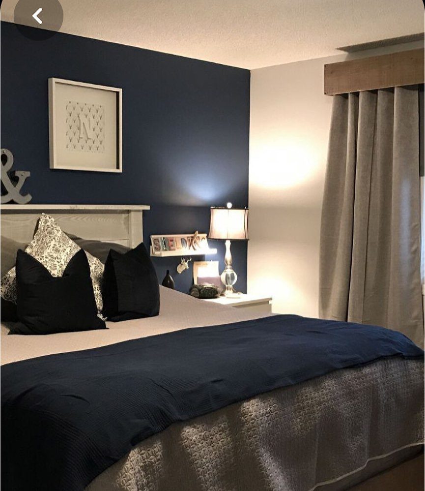 Navy blue accent wall behind a bed with dark blue pillows and a bedside lamp.
