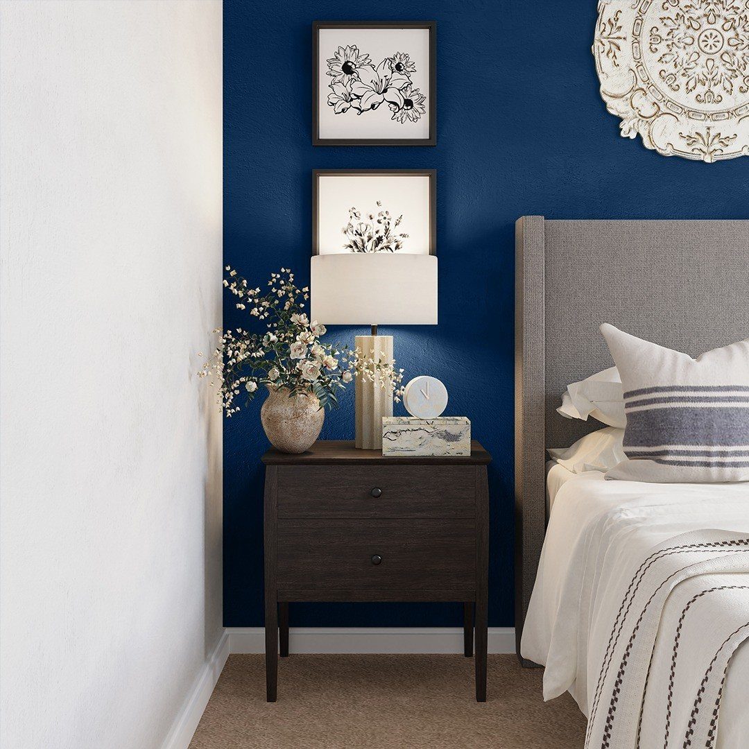 Royal blue accent wall behind a dark wood nightstand with a lamp and white flowers.