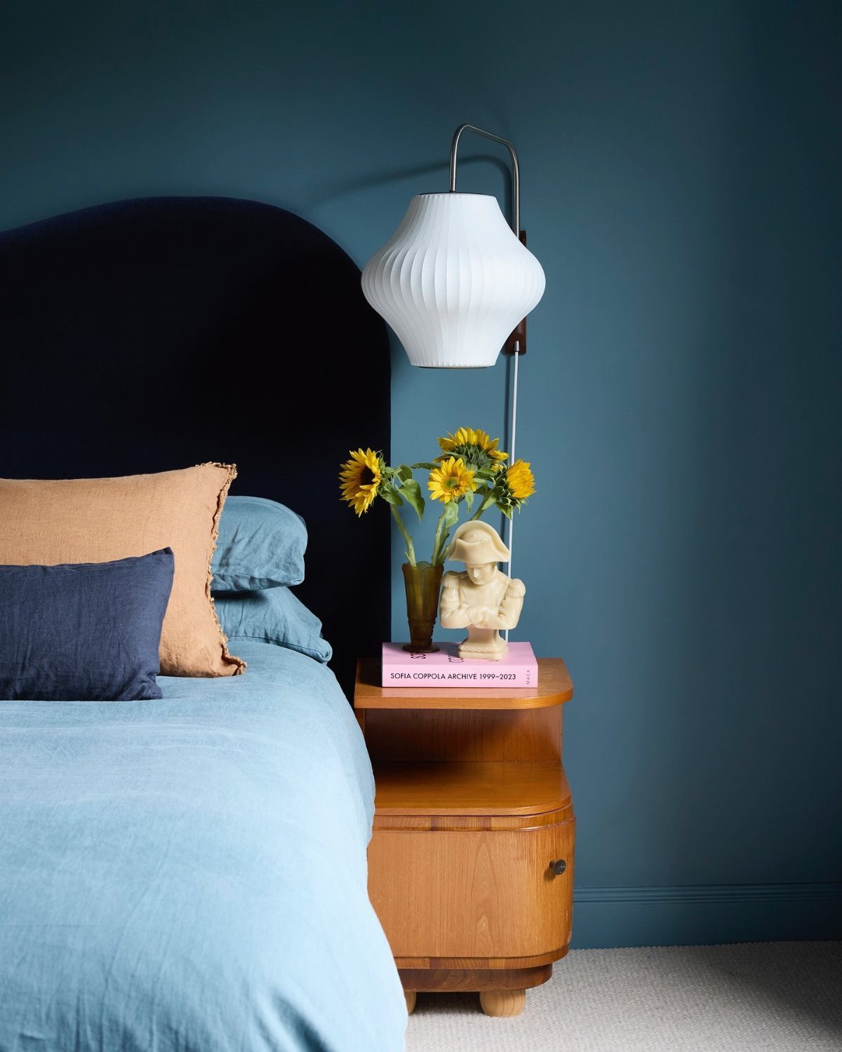 A bed with light blue linens and a navy headboard against a saturated blue wall.