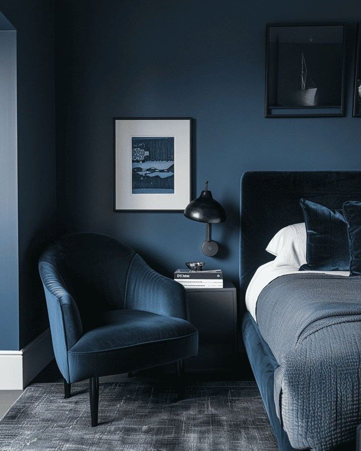 Monochromatic deep blue bedroom featuring a velvet armchair, bed, and matching dark blue walls.