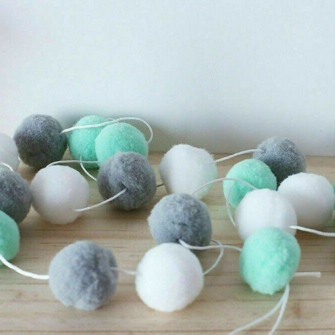 Blue, white, and grey felt pom-pom garland lying on a wooden surface.