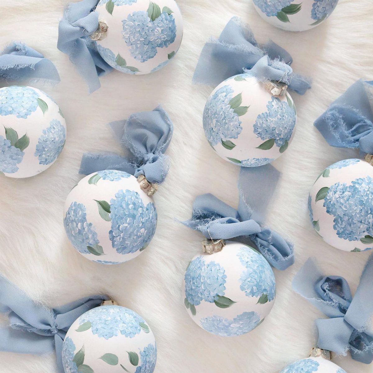 White Christmas ornaments with blue hydrangea patterns and light blue bows on white fur.