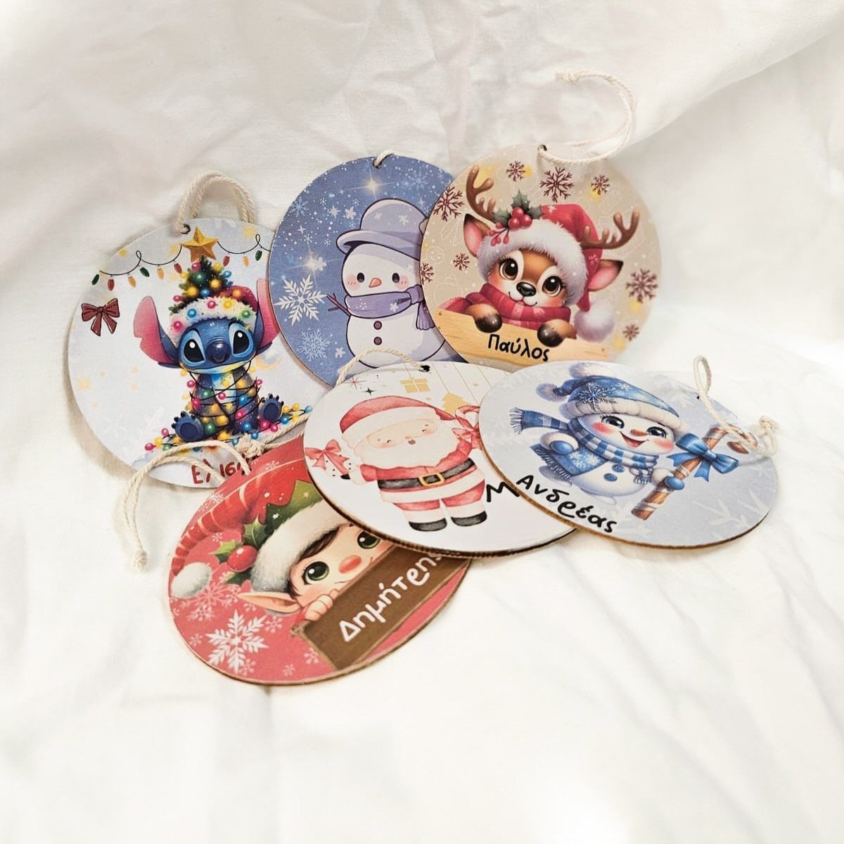 Personalized cartoon character ornaments with names written in Greek on a white fabric background.