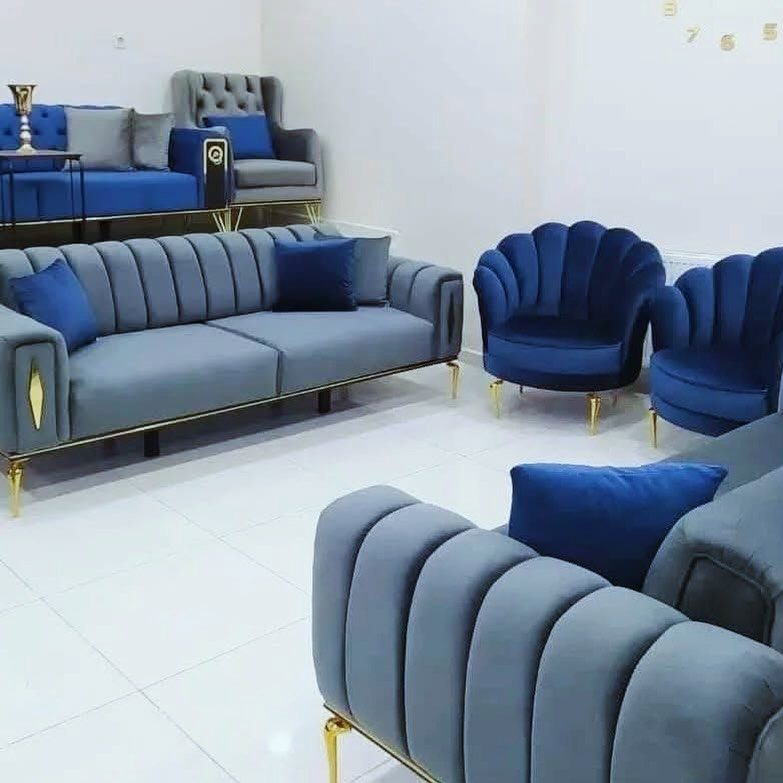 Blue and grey velvet channel-tufted sofas and armchairs with gold legs in a white room.