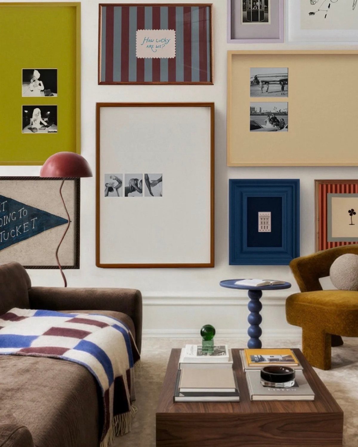 Framed artworks in various colors hanging on a white wall above a living room setup.