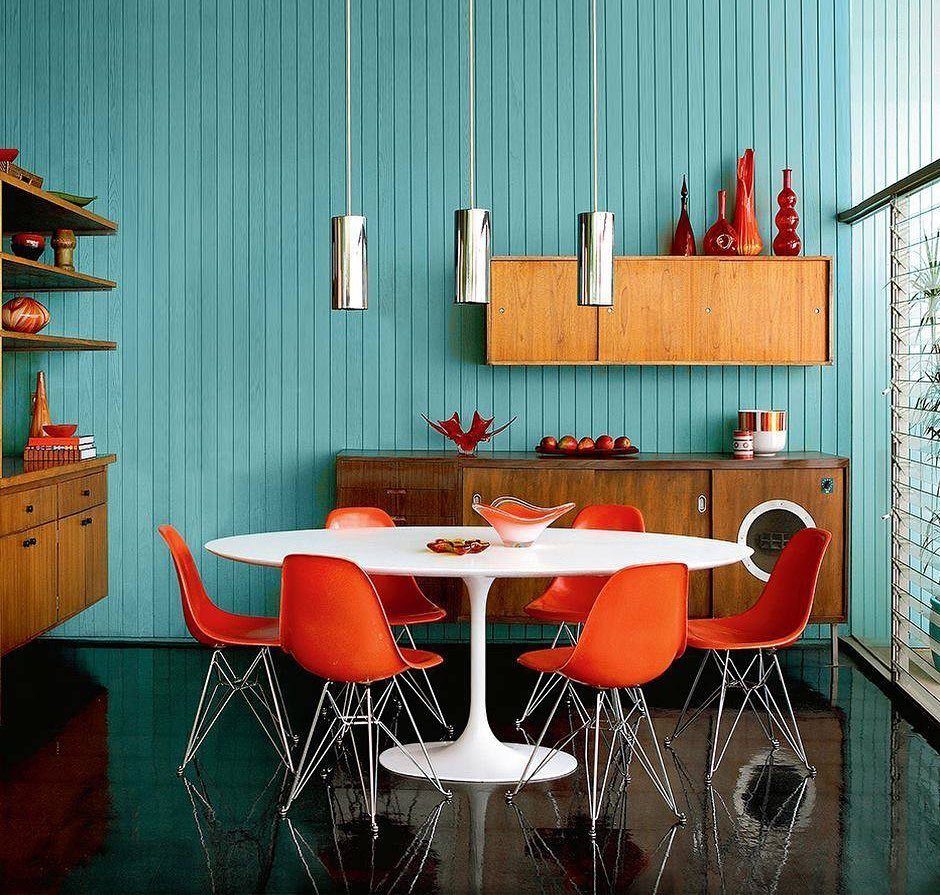 Orange dining chairs and red decor set against teal blue paneled walls.