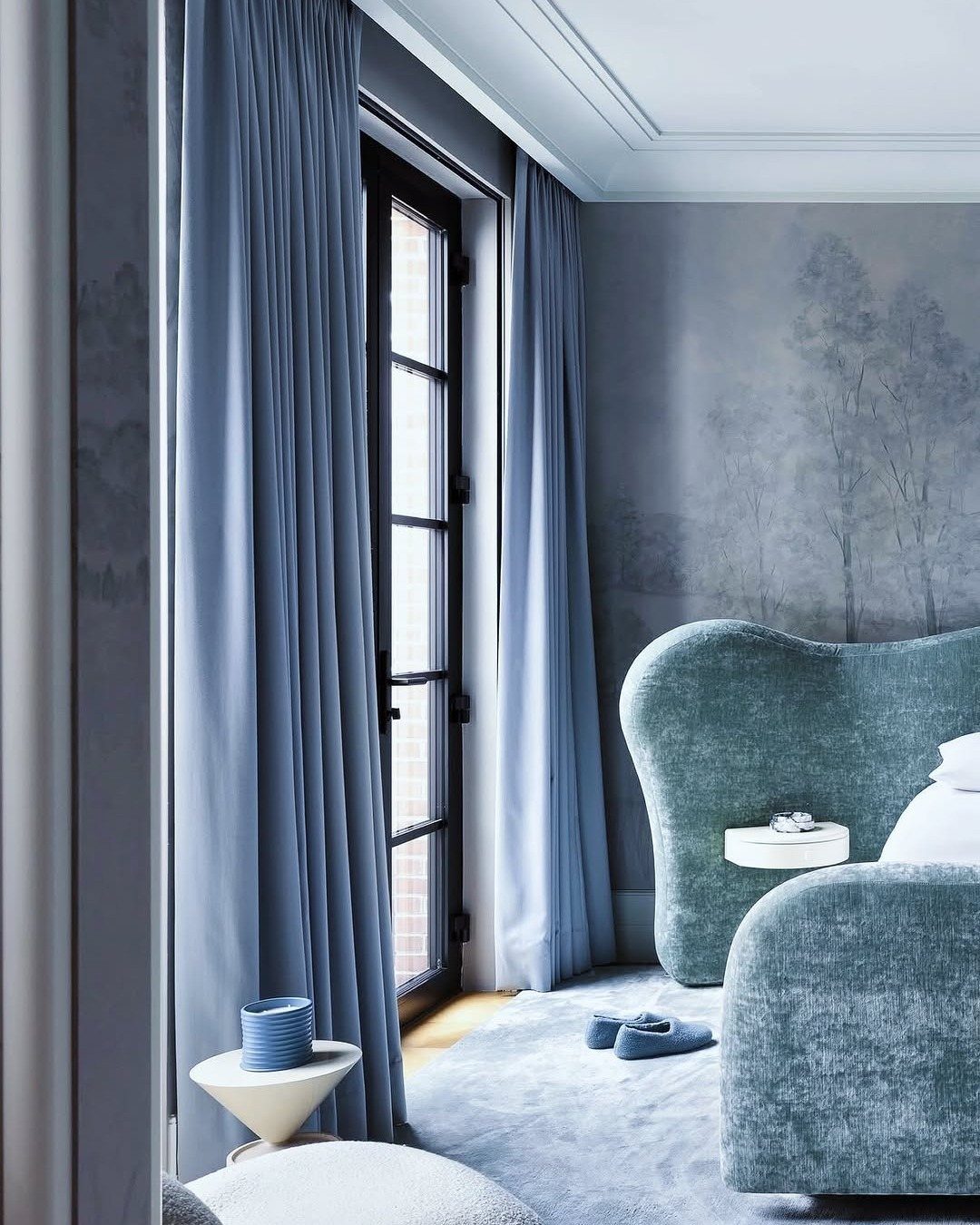 Blue curtains and a teal velvet headboard in a monochromatic blue bedroom setting.