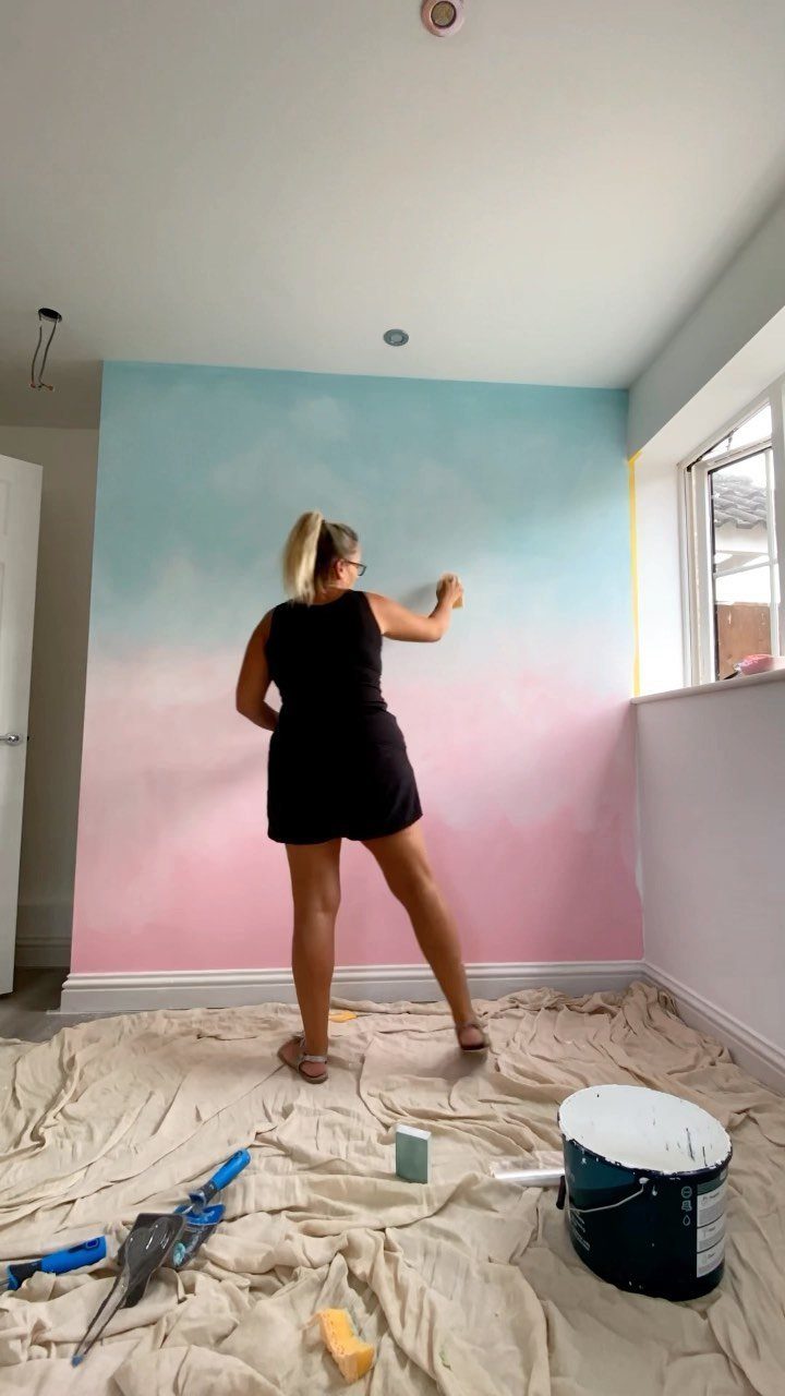 Woman painting a blue and pink ombre gradient effect on a living room wall.