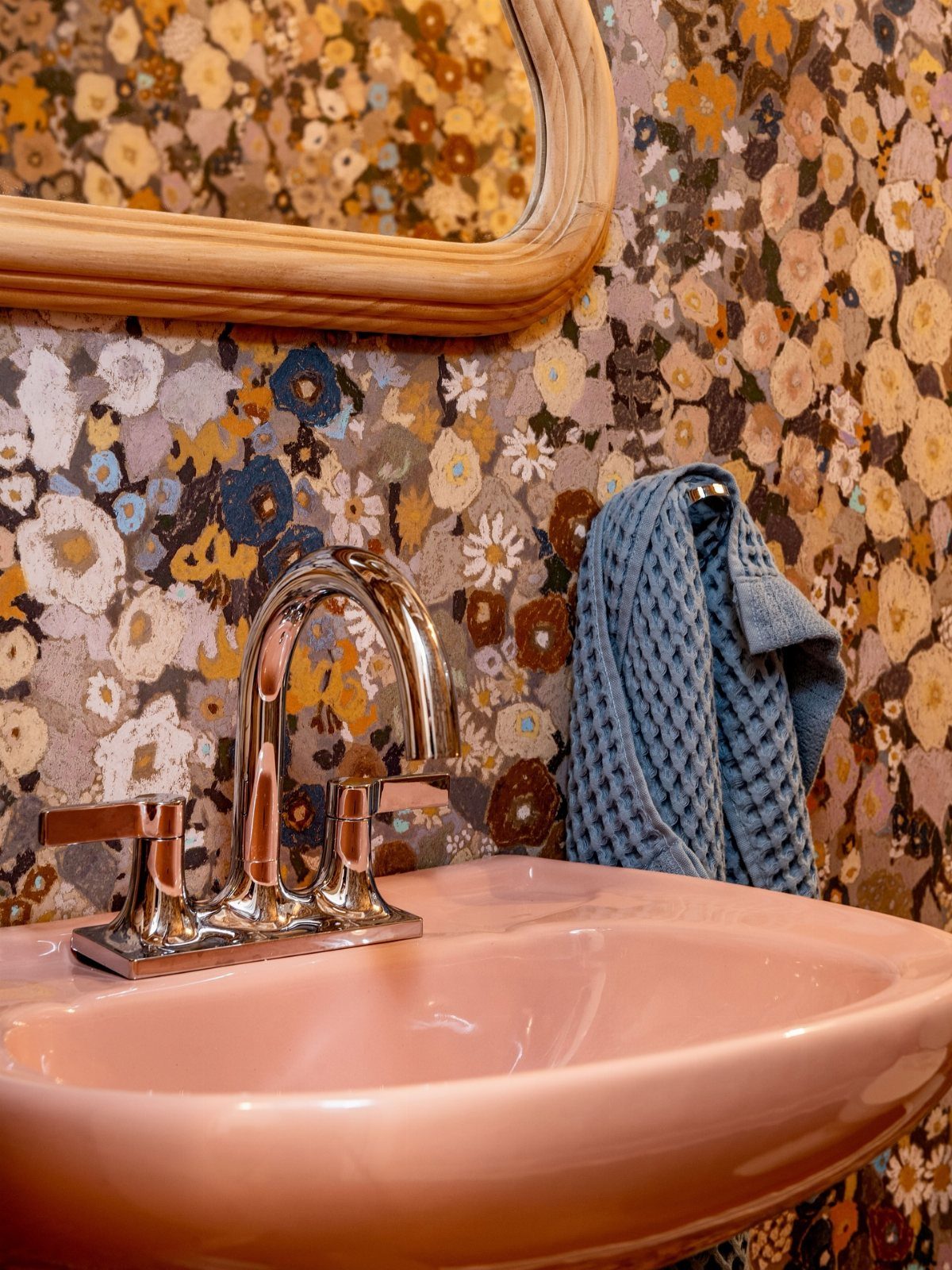 Pink ceramic sink and chrome faucet against colorful floral patterned wallpaper.