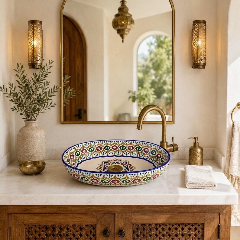 A colorful patterned ceramic vessel sink sits on a marble countertop with gold fixtures.
