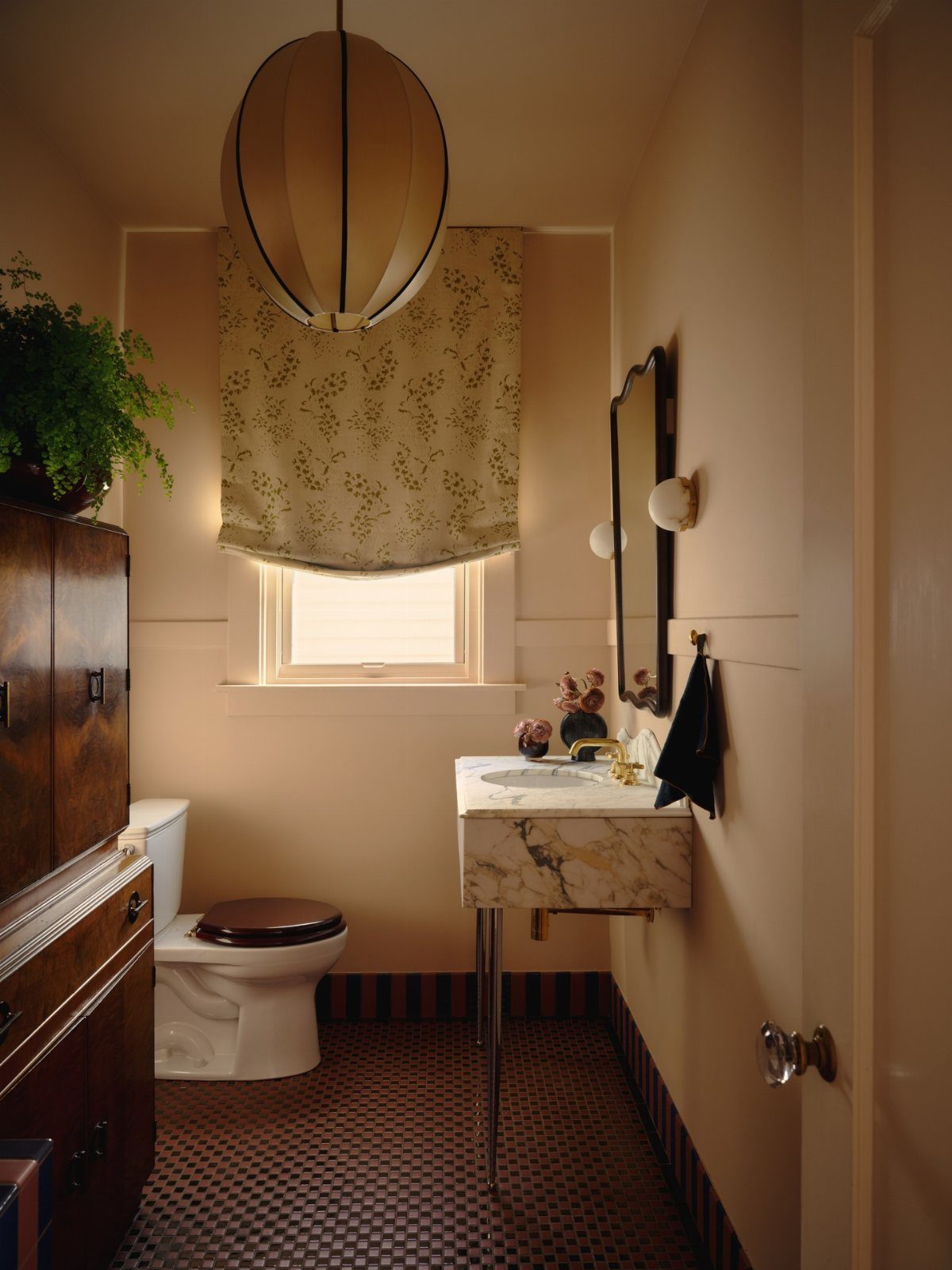 A small bathroom with patterned flooring, floral window shades, and a marble sink.