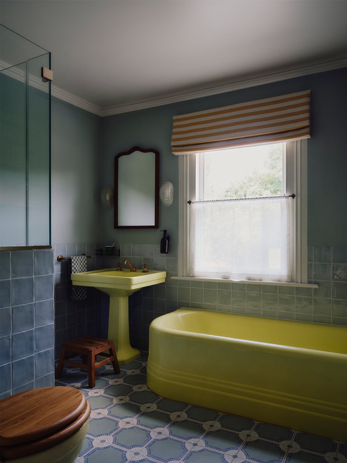 Yellow pedestal sink and bathtub set in a blue tiled bathroom with patterned floors.