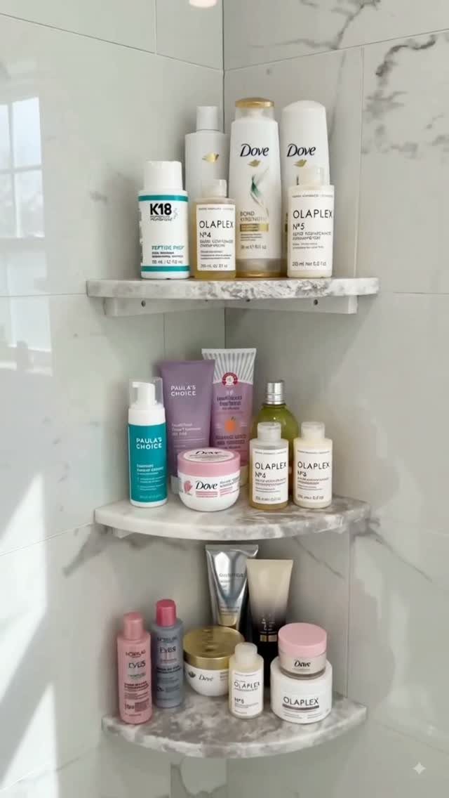 Three marble corner shelves mounted on a marble wall holding various hair care products.