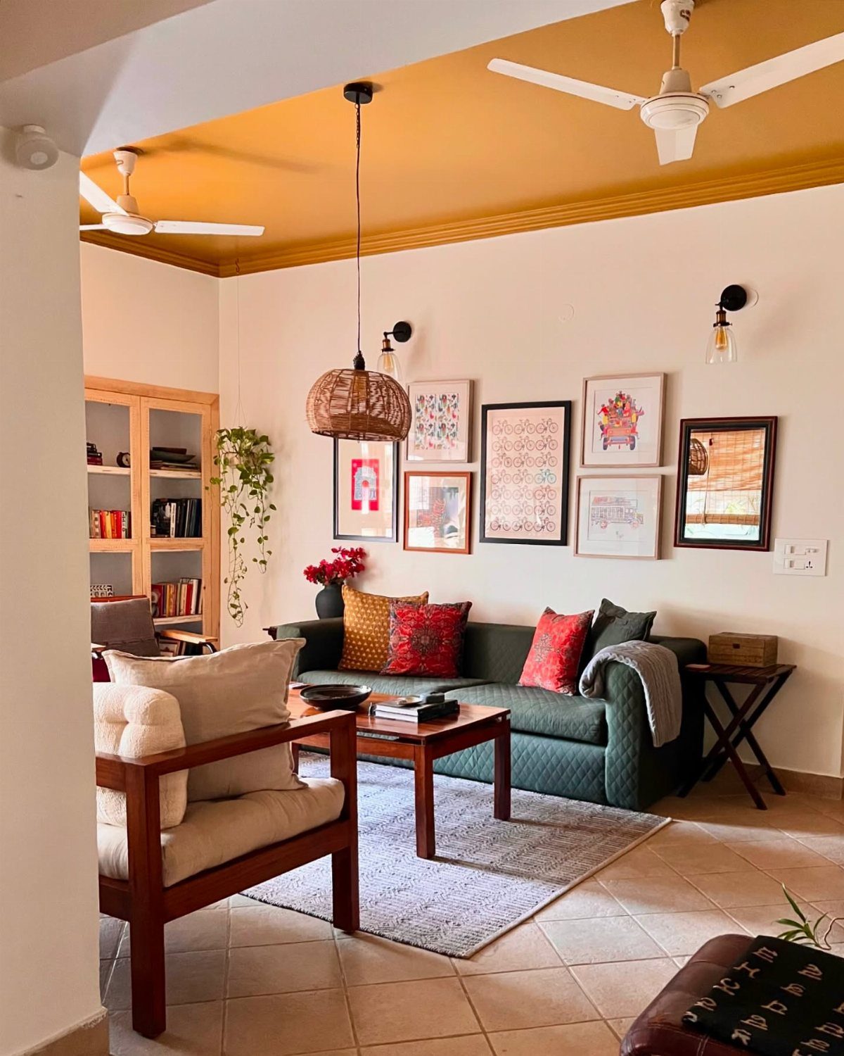 A living room with a mustard yellow accent ceiling, green sofa, and gallery wall.