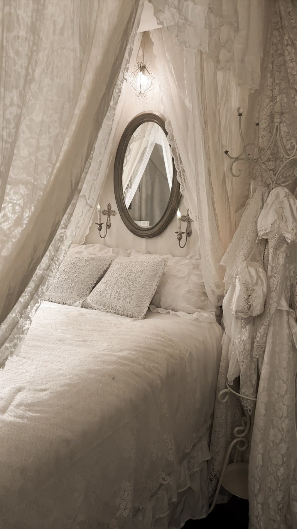 White canopy bed with sheer ruffled fabric and textured pillows in a bright room.