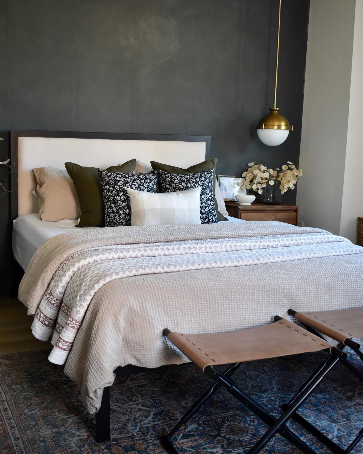 Layered bedding with textured white duvet, patterned throw, and various olive and floral pillows on a bed.