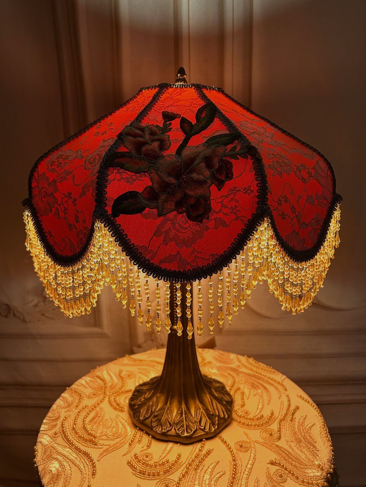 Vintage red lace lamp with black floral embroidery and hanging yellow crystal beads on a gold table.