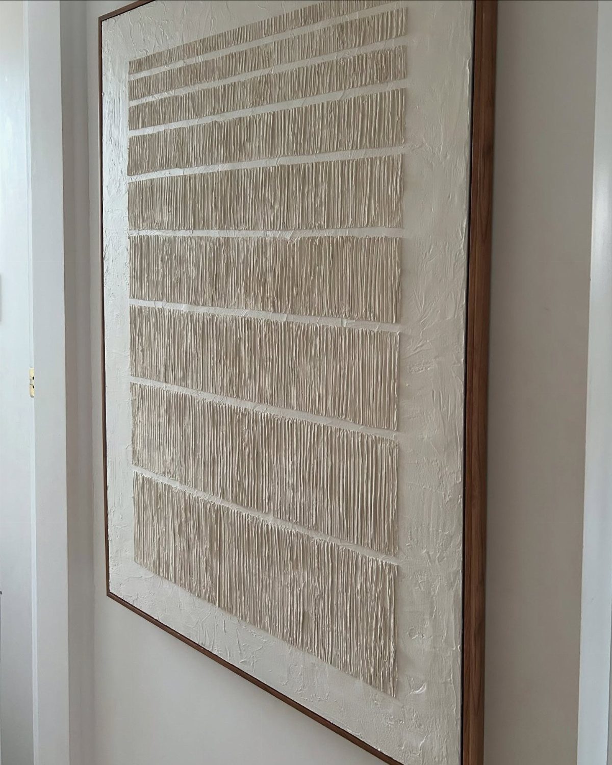 Textured beige wall art with horizontal bands of vertical ridges in a wooden frame.