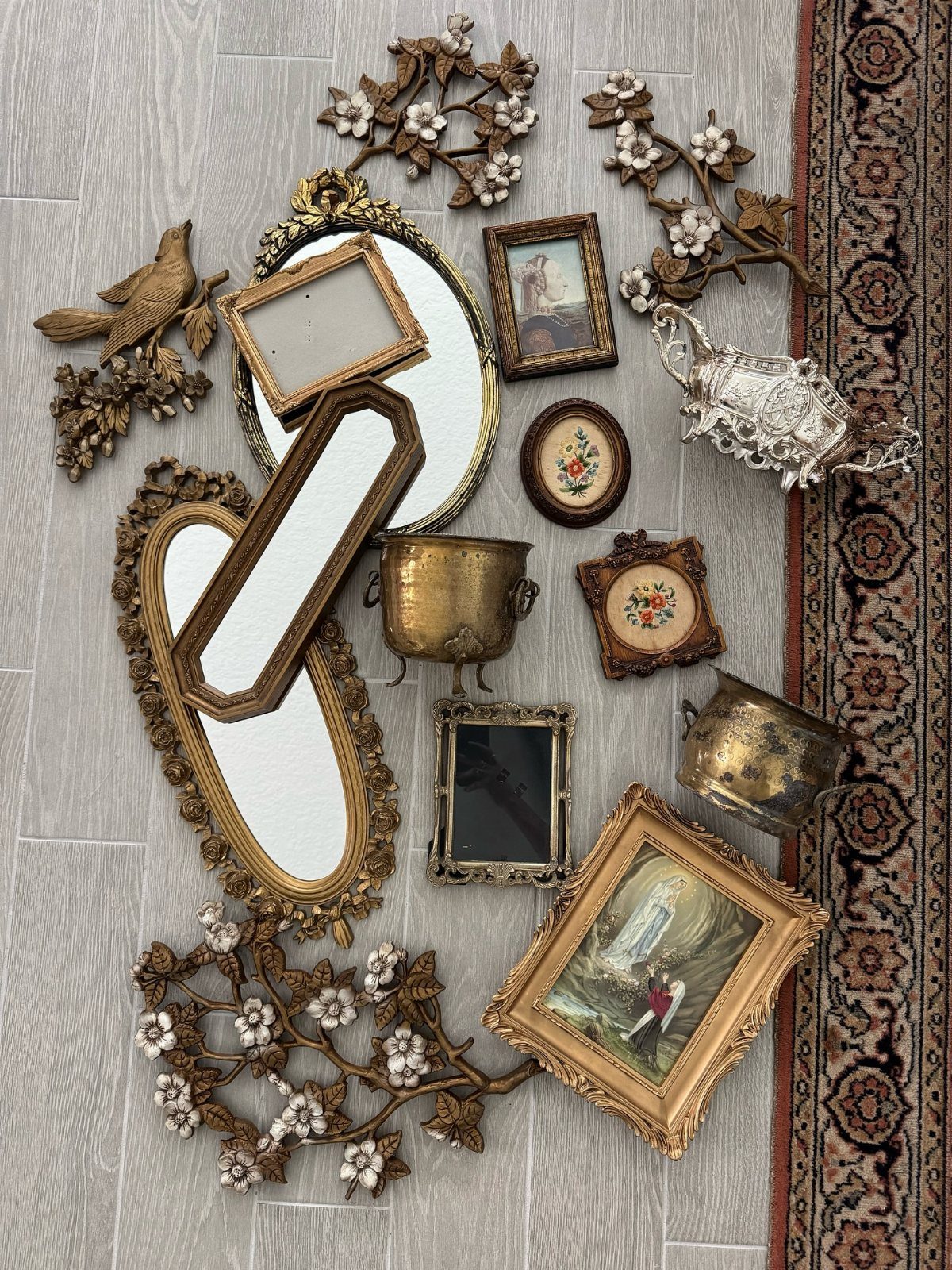 Vintage gold mirrors, framed art, and brass vessels arranged on a light grey floor.