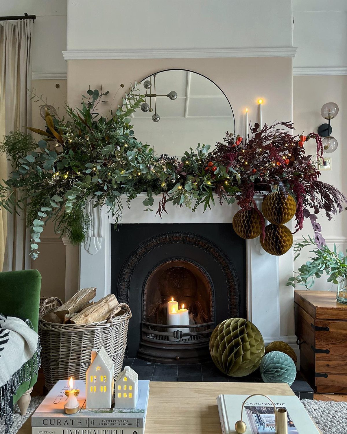 Greenery and red foliage garland with fairy lights and honeycomb ornaments decorating a fireplace mantle.