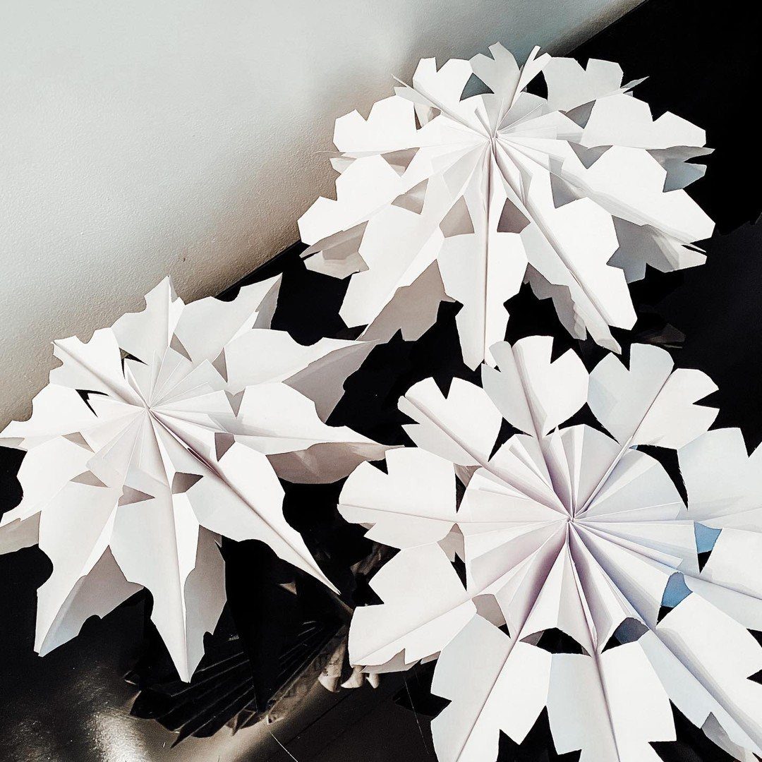 Three large white paper snowflakes crafted from folded paper bags on a dark surface.