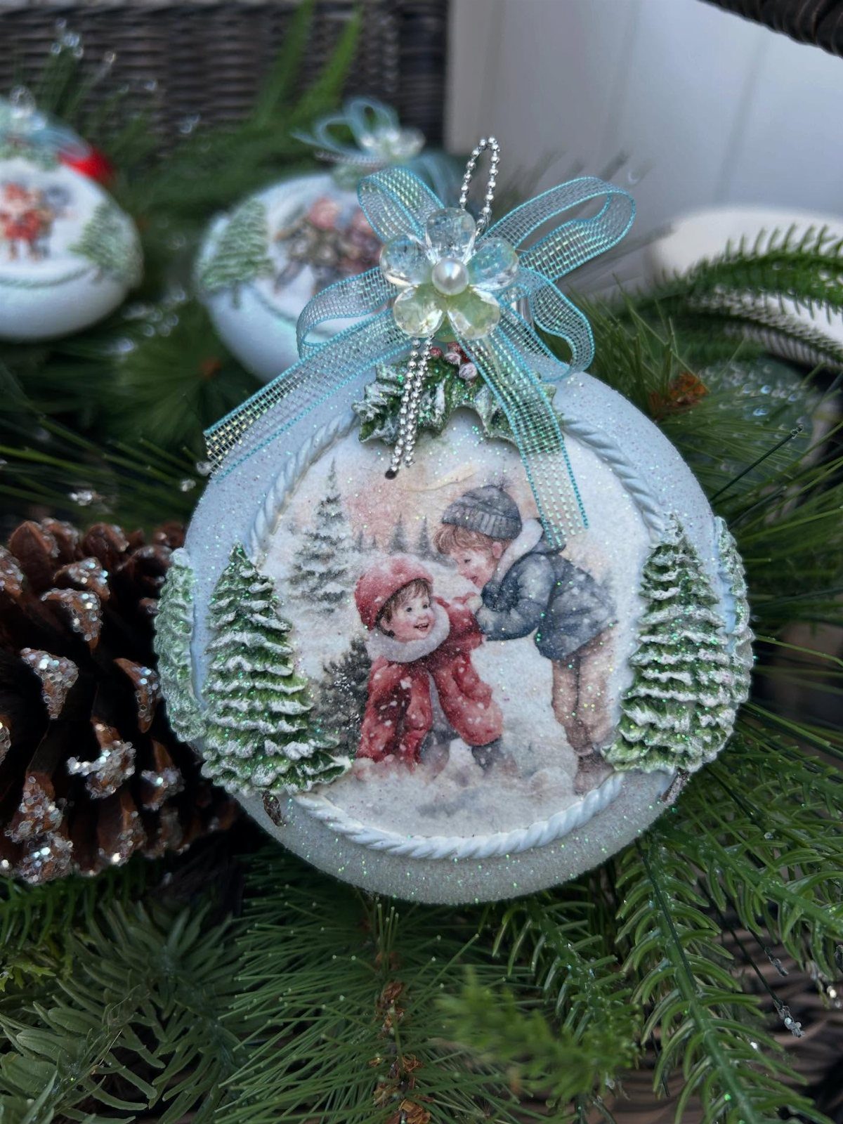 A vintage-style light blue Christmas ornament with a teal bow nestled in green pine branches.