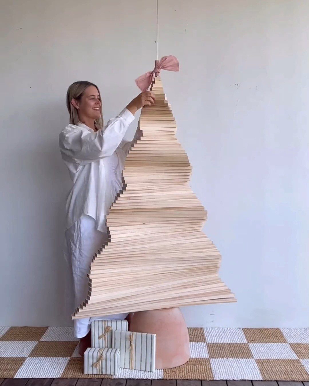 A woman standing beside a large wooden plank Christmas tree on a terracotta base.