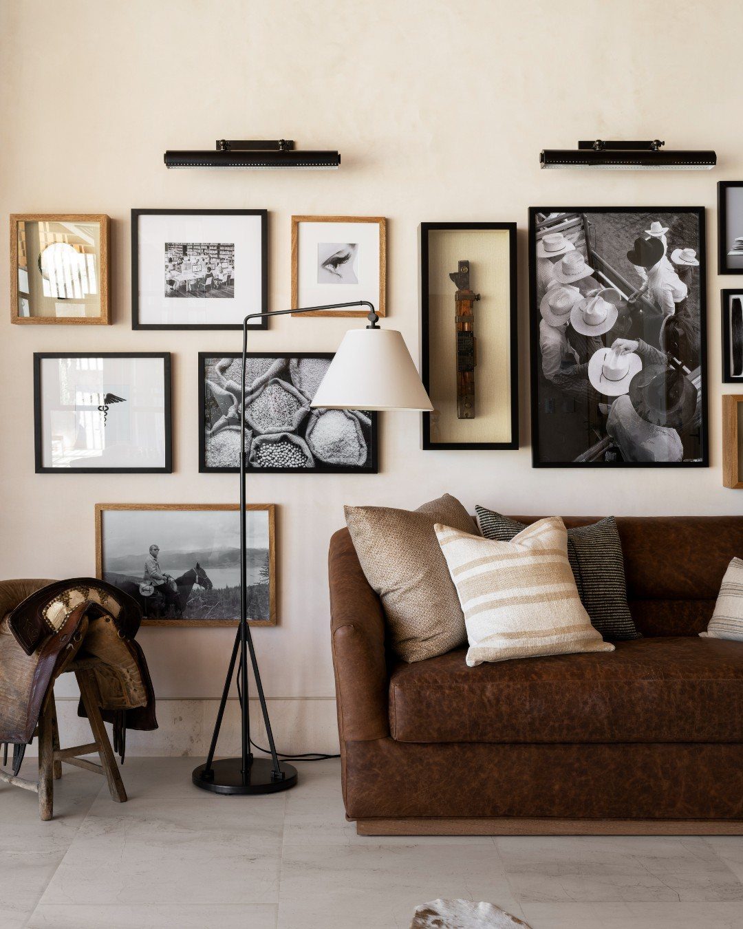A collection of black and white framed art pieces arranged in a gallery wall above a leather sofa.