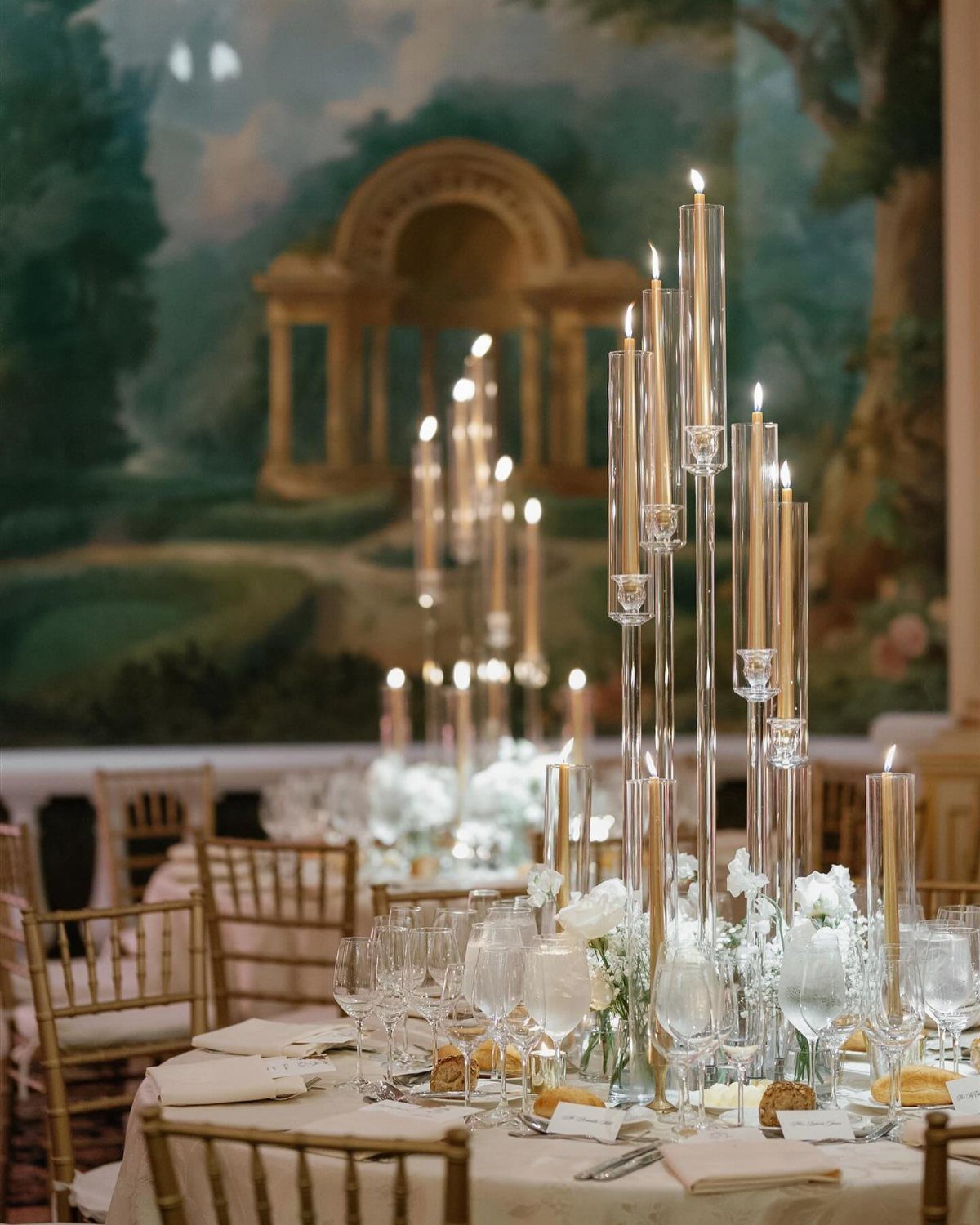 Tall glass taper candle holders with lit candles serve as elegant centerpieces on a dining table.
